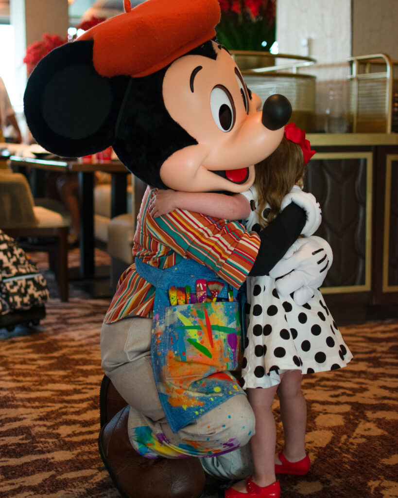 little girl in polka dot dress hugs mickey mouse at topolino's terrace character breakfast located at walt disney world's riviera resort 